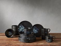 a wooden table topped with lots of black plates and cups on top of each other