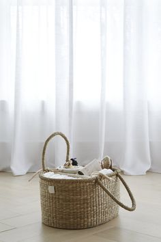 a baby in a wicker bassinet on the floor next to a window