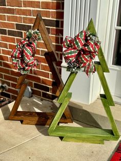 two wooden christmas trees with bows on them sitting in front of a brick wall and door