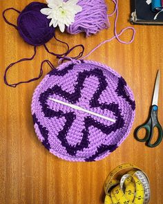 a purple crocheted bag sitting on top of a wooden table next to scissors and measuring tape