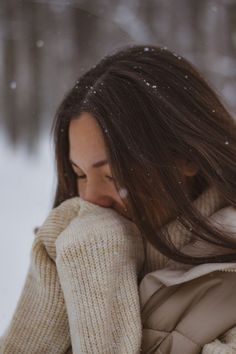 a woman with long brown hair wearing a white coat and holding her hands to her face