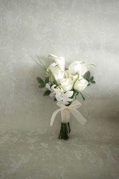 a bouquet of white flowers with green leaves on a gray background and ribbon tied around it