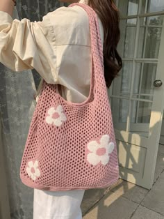 a woman carrying a pink crocheted bag with flowers on it's side