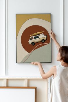 a woman pointing at a painting with a van on the road in front of it