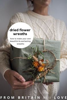 a woman holding a wrapped present with flowers on it and the words dried flower wreaths to make or buy