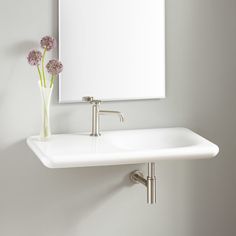 a white sink sitting under a mirror next to a vase with purple flowers in it