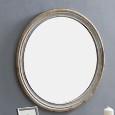 a round mirror sitting on top of a wall next to a white vase and candle