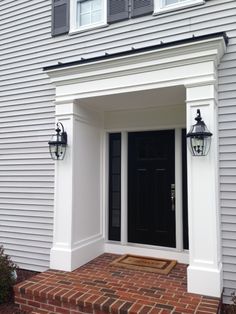 a white house with black front door and two lanterns on the side of the building