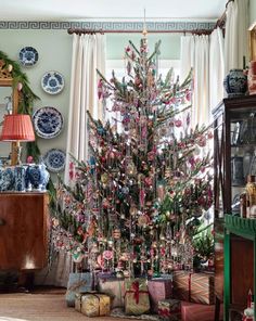 a decorated christmas tree in the corner of a room with plates on the wall and windows