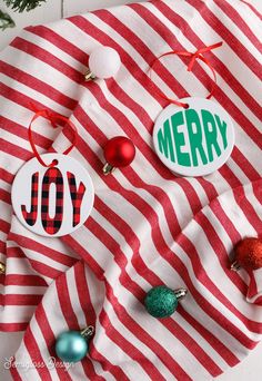 three christmas ornaments on top of a red and white striped cloth with the words merry