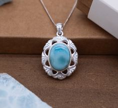 Adorn yourself with the ethereal beauty of nature embodied in our Silver Flower Pendant. This exquisite piece features a captivating oval Larimar stone nestled within an intricately crafted silver frame, reminiscent of a blooming flower in full splendor. Oval Larimar Center Stone: At the heart of this enchanting pendant lies a mesmerizing oval Larimar stone, exuding the serene blue hues and captivating patterns characteristic of this rare gem. The stone serves as the focal point, drawing the eye with its natural allure. Oval Silver Frame with Cut-Out Triangle Shapes: Surrounding the oval Larimar stone is a delicate silver frame meticulously fashioned into the shape of a flower. The frame is adorned with charming cut-out triangle shapes, enhancing the pendant's floral motif and adding depth Oval Larimar Jewelry For Anniversary, Larimar Cabochon Jewelry Gift, Oval Blue Larimar Jewelry, Oval Cabochon Necklace With Nature-inspired Style, Gift Necklaces With Oval Cabochon Natural Stones, Oval Cabochon Natural Stone Jewelry Gift, Oval Cabochon Necklaces With Natural Stones For Gifts, Teardrop Larimar Jewelry Gift, Turquoise Oval Cabochon Jewelry For Gifts