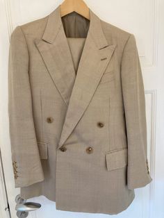 A classic, double-breasted tan suit by the late Edward Sexton of Savile Row 35, made of wool and silk with a stunning herringbone pattern. The iconic, large lapels and roped shoulders alongside details such as hand-sewn buttonholes. The trousers feature two side adjusters and have no pleats. The condition is excellent. Truly a unique and one-of-a-kind suit. An Edward Sexton suit begins at about 5000 euros.  Shoulders: 41cm - 16 inches Sleeve length: 61cm (with 3cm of fabric to let out) - 24 inch Timeless Double-breasted Buttoned Suit, Timeless Double-breasted Suit With Buttons, Timeless Double-breasted Suit, Fall Beige Suits With Buttons, Beige Fall Suits, Beige Fitted Double Breasted Suit With Lapel Collar, Beige Suits With Double Button Closure And Lapel Collar, Beige Suits With Double Button Closure And Suit Collar, Beige Business Suit With Double Button Closure