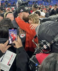 a man and woman hug each other in the middle of a large crowd at a football game