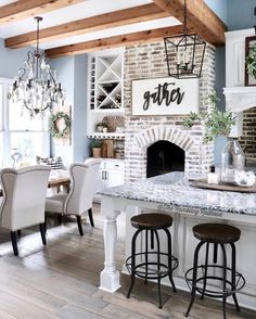 a kitchen with white chairs and a brick fireplace in the center, surrounded by wooden beams