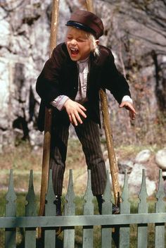 a young boy in a suit and hat climbing on a wooden fence with his hands out