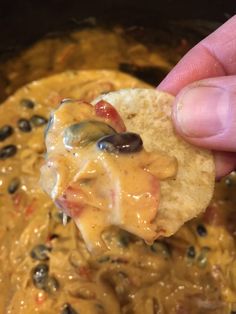 a tortilla chip being dipped with cheese and black olives in a slow cooker