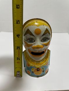 a clown mask next to a ruler on a white surface with the measuring tape in front of it