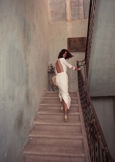 a woman is walking down the stairs in a white dress