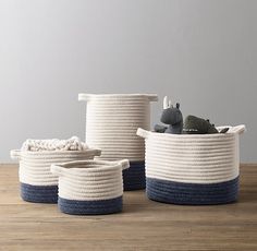 three white and blue rope baskets on a wooden table with two stuffed animals in them