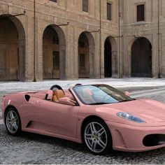 a pink sports car parked in front of a large building with arches on it's sides