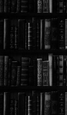 black and white photograph of many books on a book shelf in a room with dark lighting