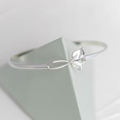 Leaf Hook Silver Bangle (available in standard and small wrist sizes) Leaf Hook bangle is one of our fabulous entry level sterling silver bangles and comes in small and standard sizes.  It's a fabulous bangle that can be worn everyday, goes with every outfit and is so easy to look after.   The ideal gift to a loved one or yourself.  This is also a perfect gift to incorporate engraving a special message inside the bracelet band to personalise the bangle to remember something, someone or a moment in time that should not be forgotten. Specification: Style:  Clasp opening  Material:  925 High Quality Sterling Silver Diameter: 65mm (standard wrist size) OR 60mm (petite wrist size) * All items are nicely packaged ready to gift in elegant jewellery boxes. * All of our items are subject to UK Hall Silver Sterling Silver Flower Bracelets, Delicate Silver Bracelet For Anniversary, Dainty Silver Flower Bracelets, Delicate Silver Round Bracelet, Delicate Sterling Silver Bracelets In Silver Color, Dainty Sterling Silver Bangle In Silver, Dainty Sterling Silver Bangle, Delicate Silver Bangle Jewelry, Delicate White Gold Bangle Bracelet