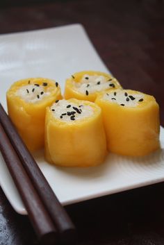 four pieces of sushi on a white plate with chopsticks next to it