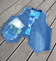 an old jean vest is sitting on a wooden floor next to a pair of jeans