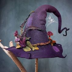 a purple witch hat with leaves and spider web on it's brim sits on top of a twig