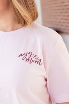 Show your Aggie pride with this stylish Texas A&M Pink Cursive Aggie Mom T-Shirt! It features a light pink shirt with "Aggie Mom" printed in maroon cursive on the left side of the chest. The back has "Aggie Mom" in darker pink with "Texas A&M University College Station" circling it - perfect for any proud Aggie Mom! - Brand: Bella+Canvas - 100% Cotton - Machine Wash Warm/Tumble Dry Low Pink Long Sleeve T-shirt With Text Print, Pink Long Sleeve T-shirt With Letter Print, Pink Long Sleeve T-shirt With Text, Pink Long Sleeve T-shirt With Name Print, Pink Screen Print T-shirt For Mother's Day, Pink Pre-shrunk Long Sleeve T-shirt, Pink Long Sleeve Pre-shrunk T-shirt, Mother's Day Pink Graphic Tee, Pink Tops With Text Print For Mother's Day