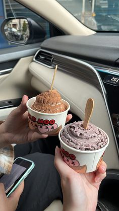 two people holding ice cream in their hands while sitting in a car with the steering wheel behind them