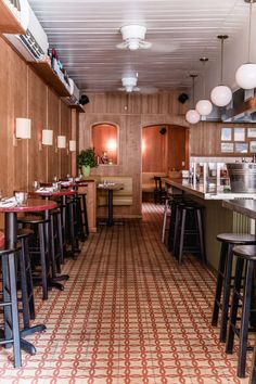 the inside of a restaurant with tables, stools and lights hanging from the ceiling