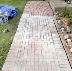 a brick walkway in front of a house with a trash can and garbage bag on the side