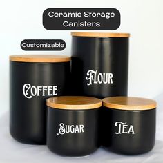 four black ceramic canisters with wooden lids and labels on them, labeled coffee, flour, sugar, tea