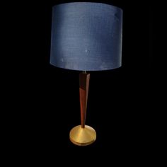 a table lamp with a blue shade on the top and gold base, against a black background