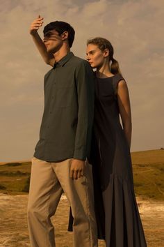 a man and woman standing next to each other on a field with clouds in the background