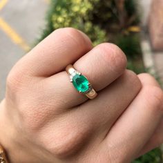 a person's hand with a green ring on top of their finger and a gold band