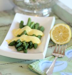 a plate with asparagus, lemon and sauce on it next to a fork