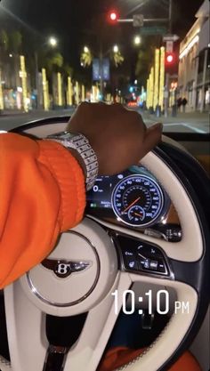 a person driving a car at night with their hand on the steering wheel while wearing an orange sweater