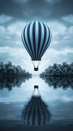 a hot air balloon floating in the sky over water with trees and clouds behind it