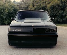 a black sports car parked in a parking lot next to some trees and bushes on the side of the road