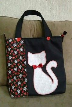 a black bag with a white cat and red bow on it sitting on a couch