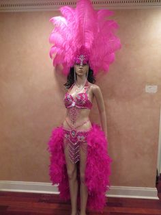 a mannequin dressed in pink feathers stands against a wall