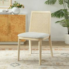 a white chair sitting on top of a rug next to a wooden cabinet and potted plant