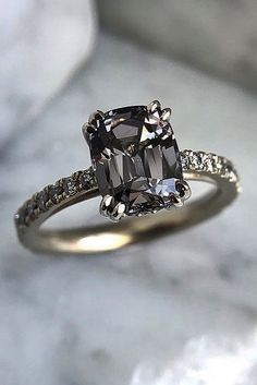 an engagement ring with a cushion cut diamond and pave diamonds on the band, sitting on a marble surface