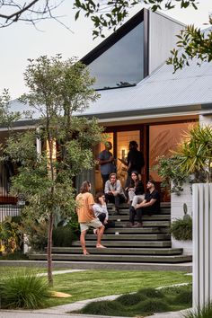 some people are sitting on the steps in front of a house and one person is standing up