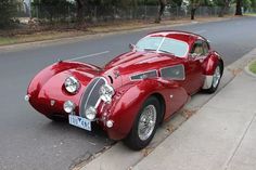 an old red sports car parked on the side of the road next to a curb