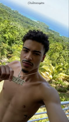 a shirtless man pointing at the camera with trees and ocean in the back ground