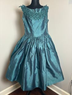 Someone custom made this pretty party dress for someone special and someone is going to get a real vintage bargain!  I can't be sure, but I think it was not factory produced. The bright teal material is a shiny, light satin like material. The waist is defined by matching piping. It is sleeveless. The rounded neckline is covered in a unique floral lace. In the center of each flower is a rhinestone. There is a major flaw  - the metal zipper in the back of the dress will not unzip. It will not be a Fitted Full Skirt Festive Dress, Festive Fitted Dress With Full Skirt, Fitted Dress With Full Skirt For Festive Season, Silk Full Skirt Evening Dress For Party, Silk Tea Length Dress For Party, Silk Tea Length Party Dress, Blue Vintage Dress For Party, Silk Tea-length Dress For Party, Silk Tea-length Party Dress