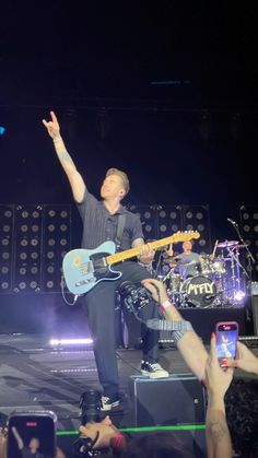 a man on stage with his arms in the air while playing an electric guitar and singing